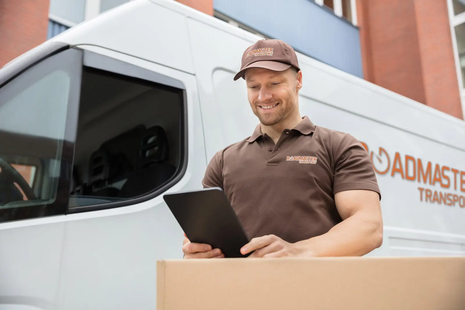 A man in brown shirt holding a laptop near box.